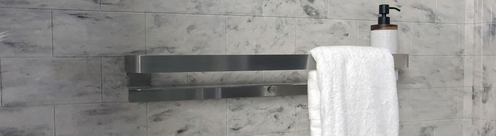 A modern bathroom features a stainless steel towel rack with a white towel hanging over it. A soap dispenser sits on the rack. The walls are marble-tiled.