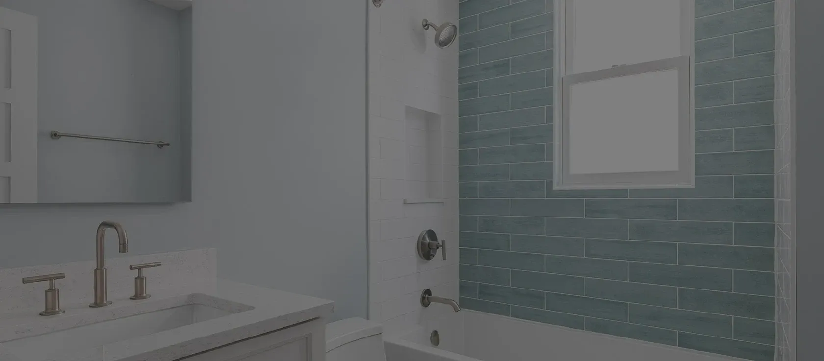 Bright bathroom with modern fixtures. Light blue walls, a white vanity with a sleek faucet, and a bathtub with teal subway tile to the right.