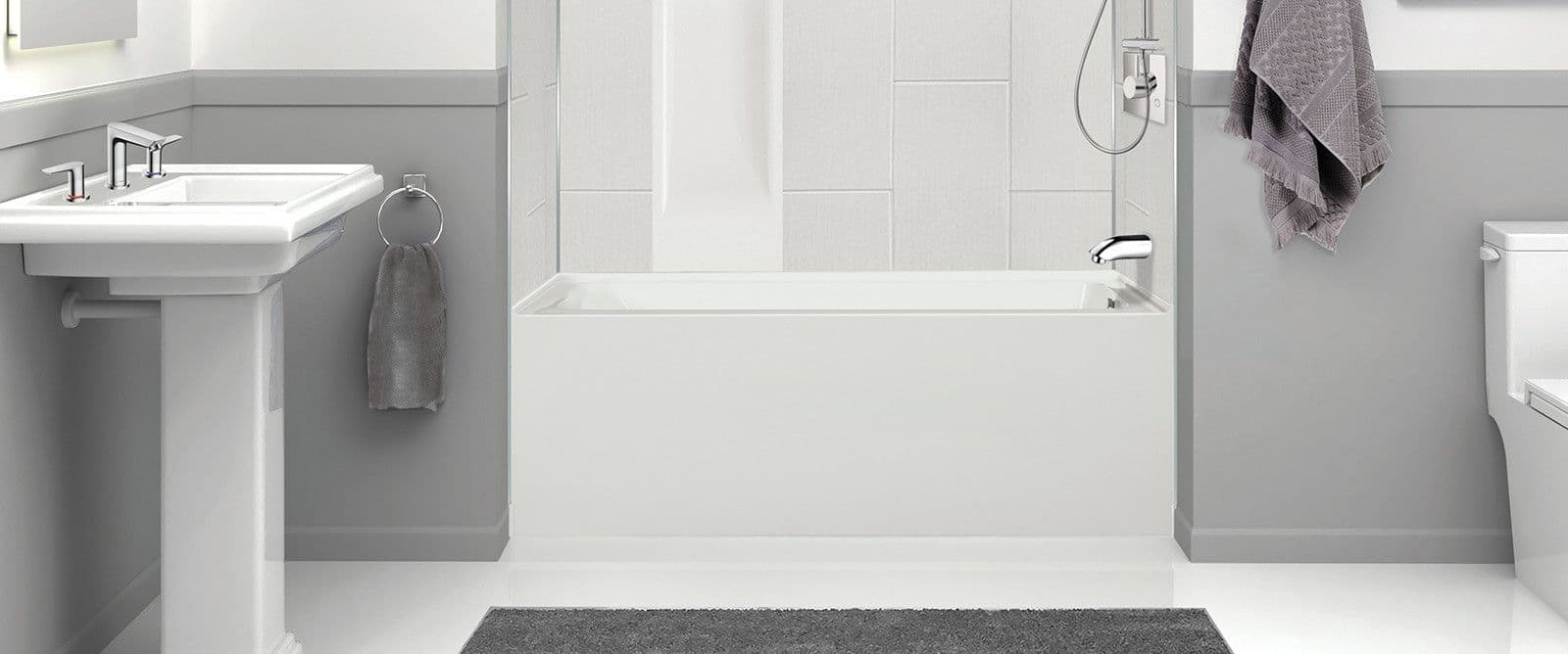 Modern gray bathroom with a pedestal sink, bathtub, towel, toilet, and gray rug on the floor.