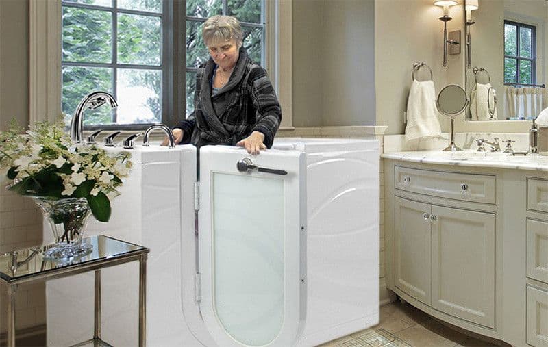 A woman in a cozy bathroom enters a modern walk-in bathtub. The room is elegantly decorated with flowers and soft lighting.