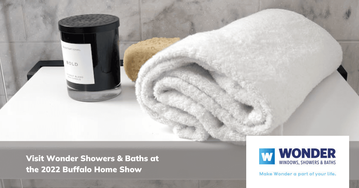 A rolled white towel, black candle, and beige sponge rest on a shelf. Text reads: "Visit Wonder Showers & Baths at the 2022 Buffalo Home Show." Logo of Wonder Windows included.