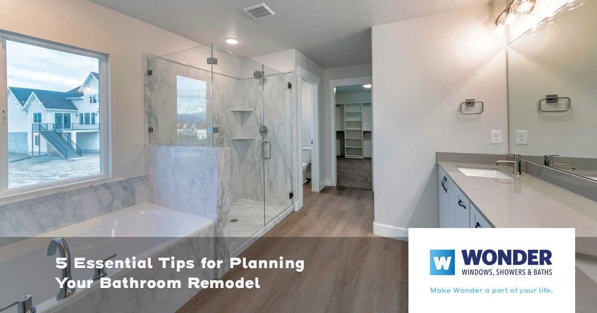 Modern bathroom with a large glass shower, marble tub, and wooden floors. The text reads "5 Essential Tips for Planning Your Bathroom Remodel." Logo: Wonder Windows, Showers & Baths.