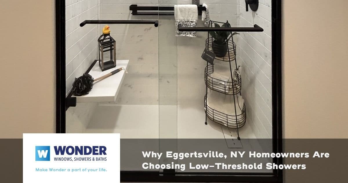 A modern low-threshold shower with white tiles, glass doors, and black fixtures. Inside, there are shower essentials and a towel. Text overlay mentions Eggertsville, NY homeowners choosing this style.