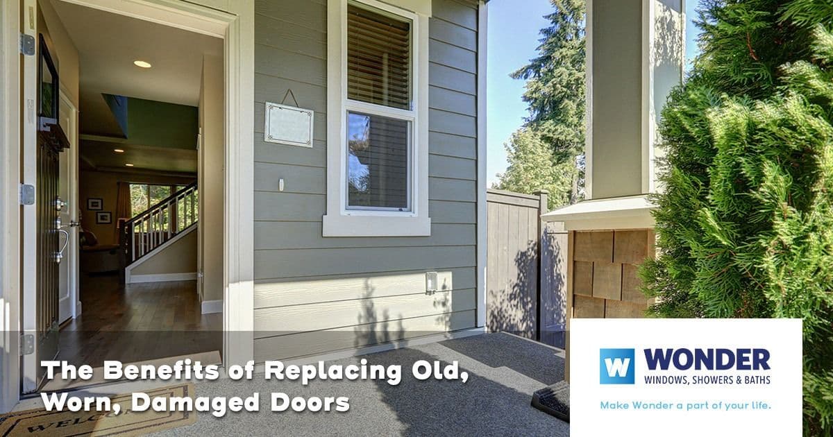 Modern home entrance with a wooden door open to a bright, inviting interior. Text reads "The Benefits of Replacing Old, Worn, Damaged Doors." Logo: Wonder Windows.