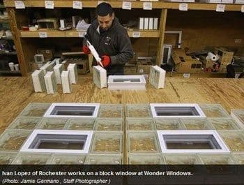 A man assembles block windows at a workshop table, surrounded by glass blocks and tools. The setting is organized, conveying focus and craftsmanship.