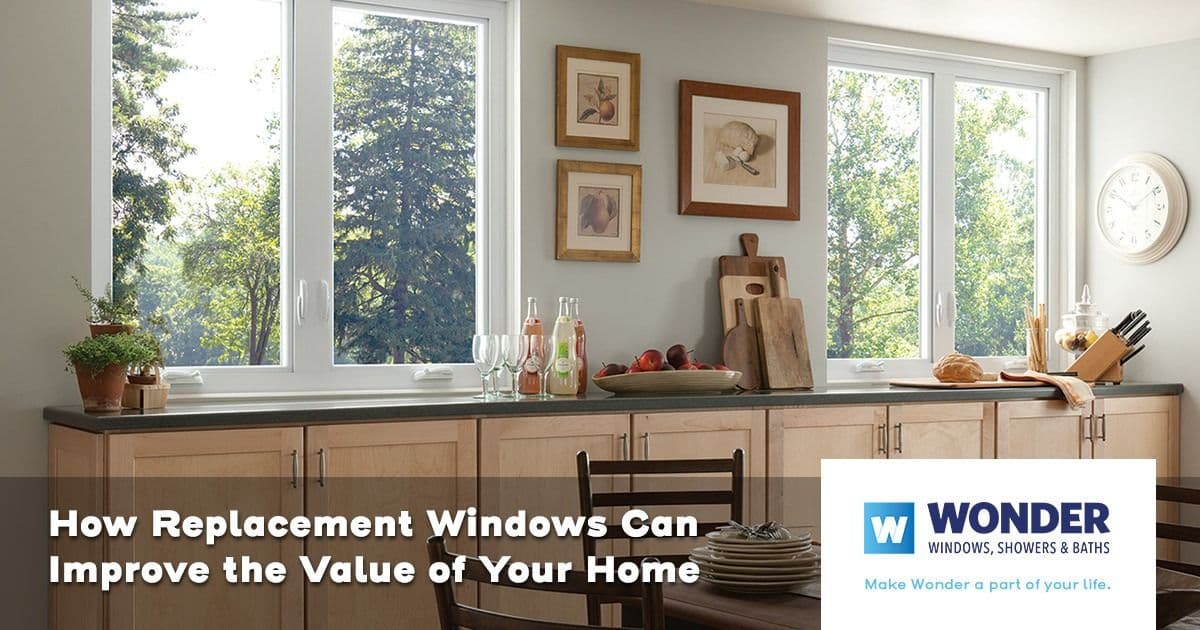 Modern kitchen with large windows showcasing a green, scenic view. Countertop has cutting boards and fruit. Text at the bottom promoting window replacement.