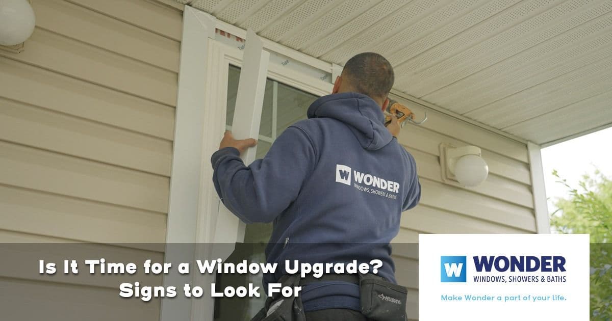 A worker in a blue hoodie installs a window on a beige house. Text reads "Is It Time for a Window Upgrade? Signs to Look For." Wonder logo in the corner.