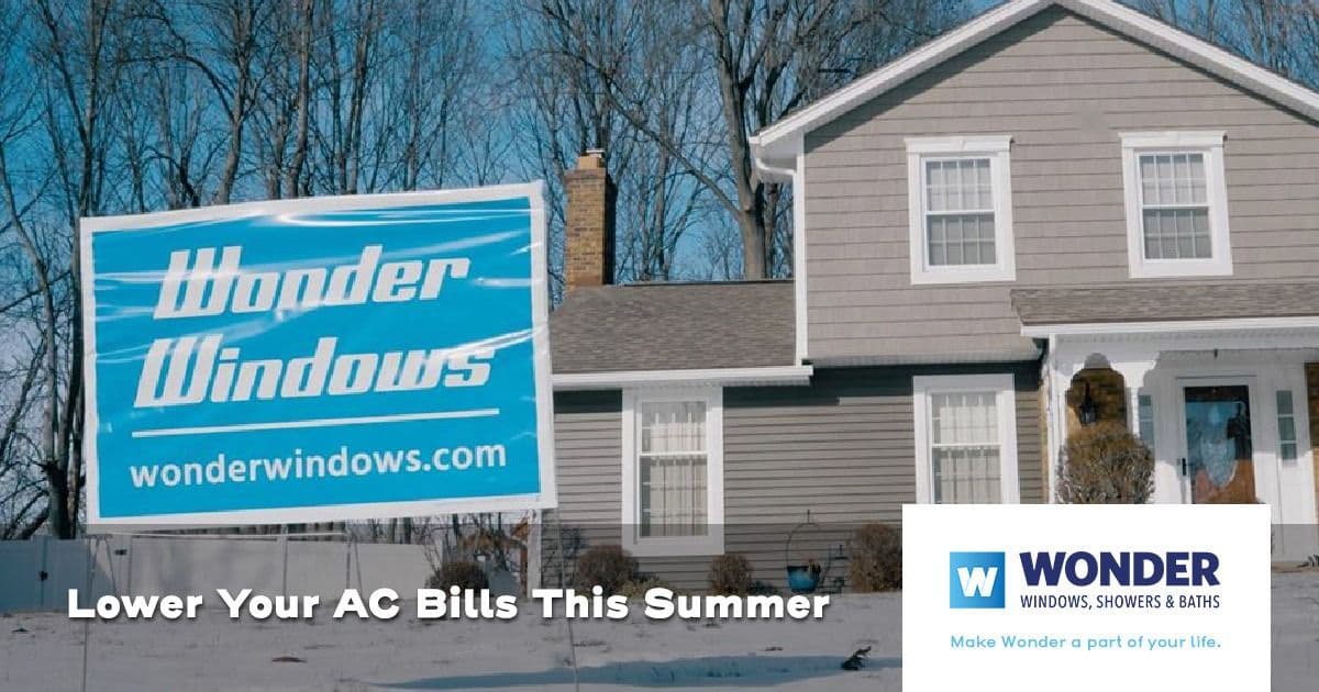 A gray house with a prominent blue "Wonder Windows" sign in the snowy yard. Text reads, "Lower Your AC Bills This Summer." The scene feels promotional.