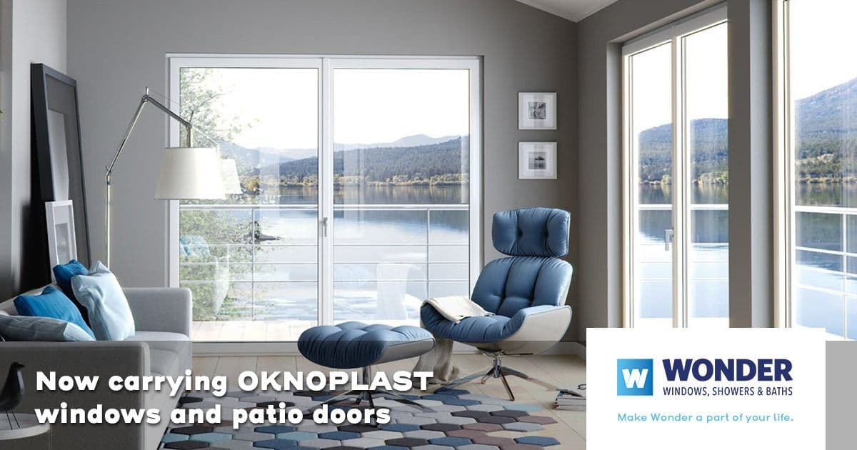 Modern living room with large OKNOPLAST windows overlooking a serene lake and mountains. A sleek chair, cushions, and modern decor convey tranquility.