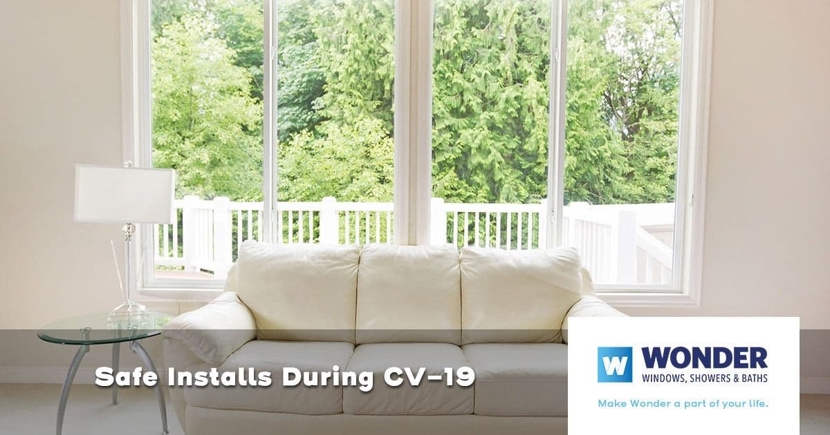 A bright living room with a white couch facing large windows showcasing a green garden. Text reads "Safe Installs During CV-19" with the Wonder logo.