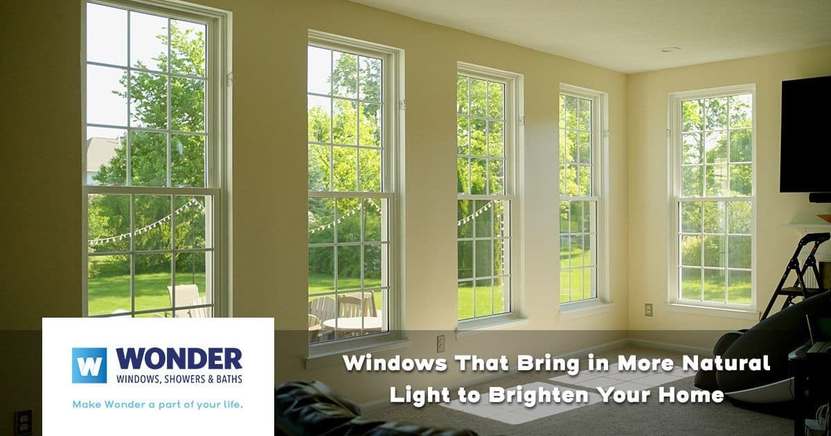 Bright room with tall windows letting in natural light, offering a view of a lush green yard. Text promotes windows enhancing home brightness. Logo for Wonder Windows.