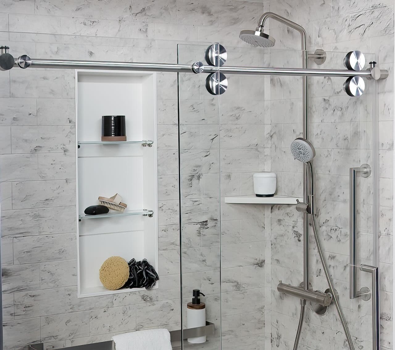 Modern shower with glass doors and chrome fixtures against marble tiles. Features a rain showerhead, handheld sprayer, and recessed shelves holding toiletries.