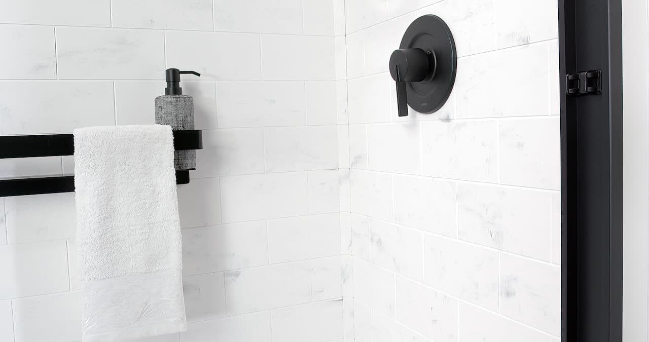 Modern bathroom shower with black fixtures against white marble-tiled walls. A towel hangs on a black bar, creating a sleek, minimalist look.
