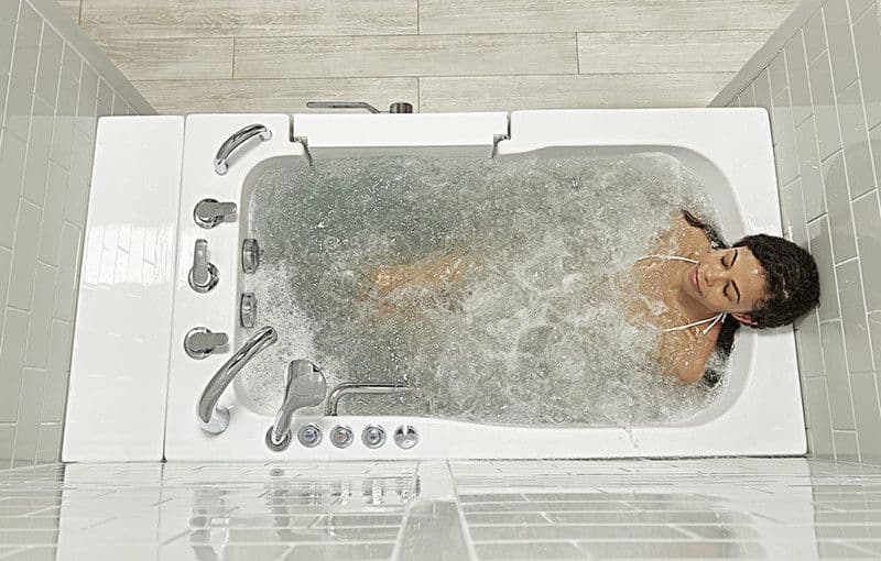 A woman relaxes in a modern, bubbly white bathtub, eyes closed, exuding tranquility. The bathroom features light tiles and sleek fixtures.