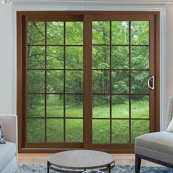A cozy living room features a large sliding glass door with wooden frames, revealing a lush, green forest outside.