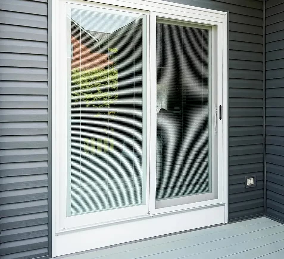 Sliding glass patio door with built-in blinds, framed by dark gray siding.